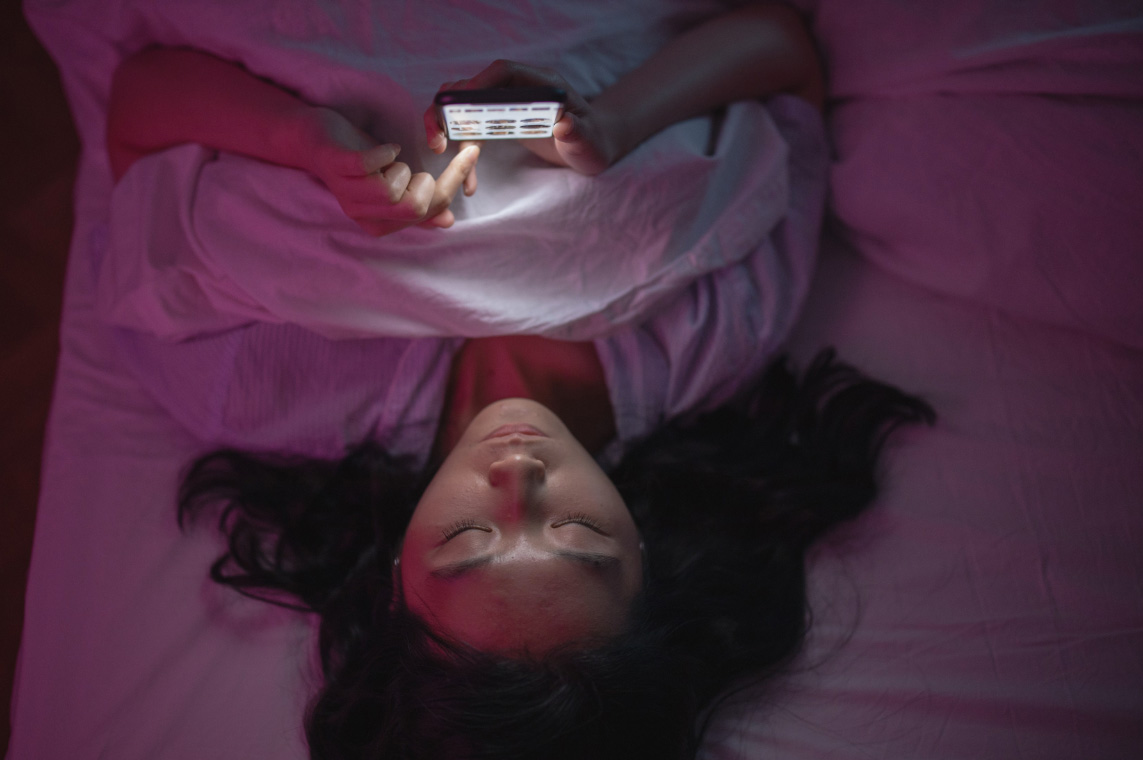 Woman lying in bed at night scrolling her phone